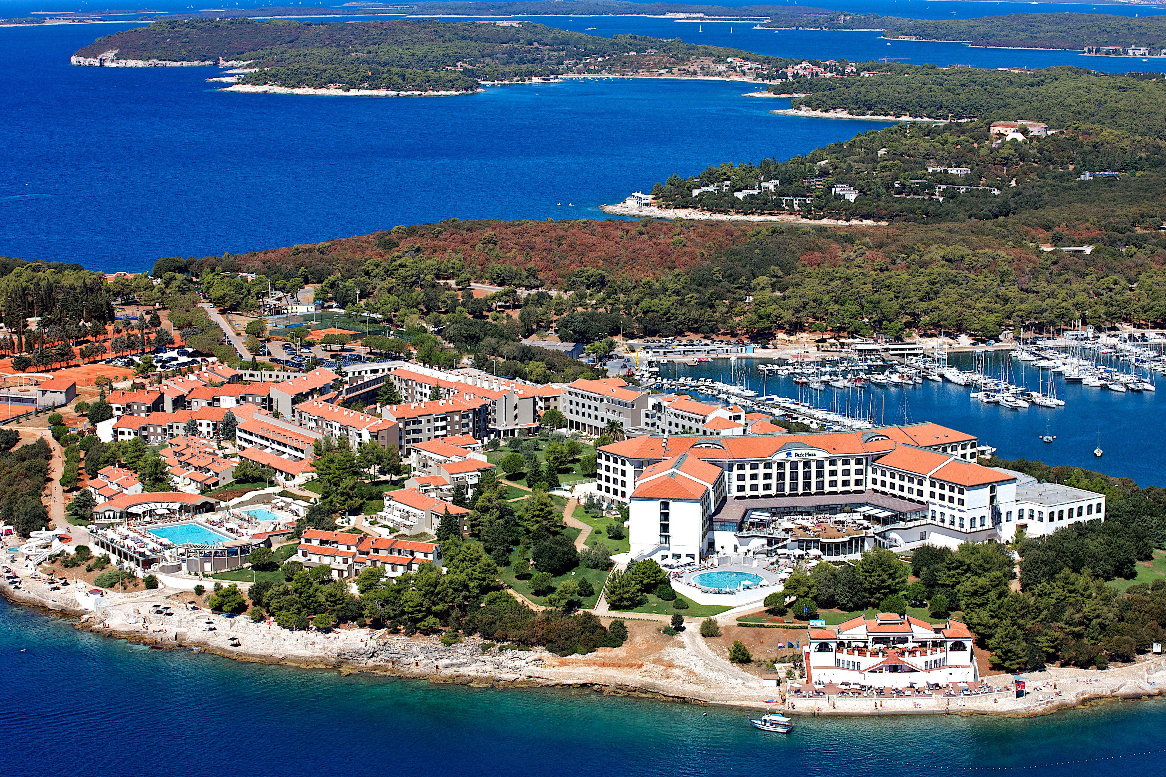 An aerial view of a coastal resort with multiple buildings, a marina, and a large swimming pool.