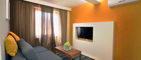 A modern living room with a sofa, a coffee table, and a flat-screen TV mounted on a white wall.