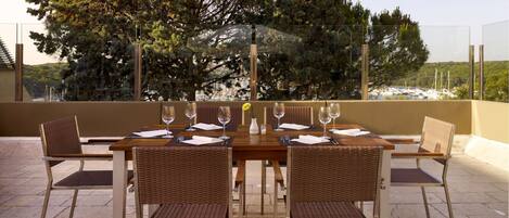 A dining table set with six chairs, a vase with a yellow flower, and wine glasses.