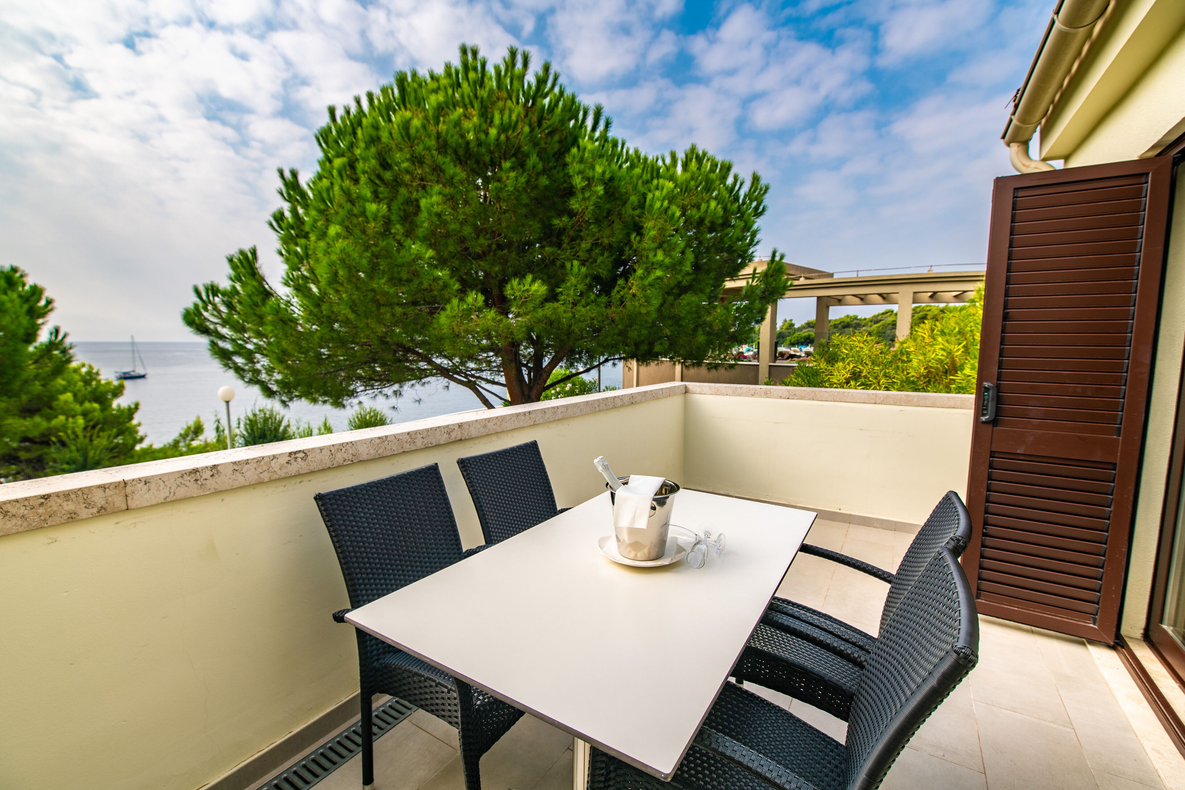 Ein Balkon mit Tisch und Stühlen, der auf ein Gewässer und einen Baum blickt.