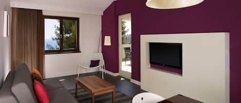 A modern living room with a sofa, a coffee table, a TV mounted on the wall, and a window with curtains.