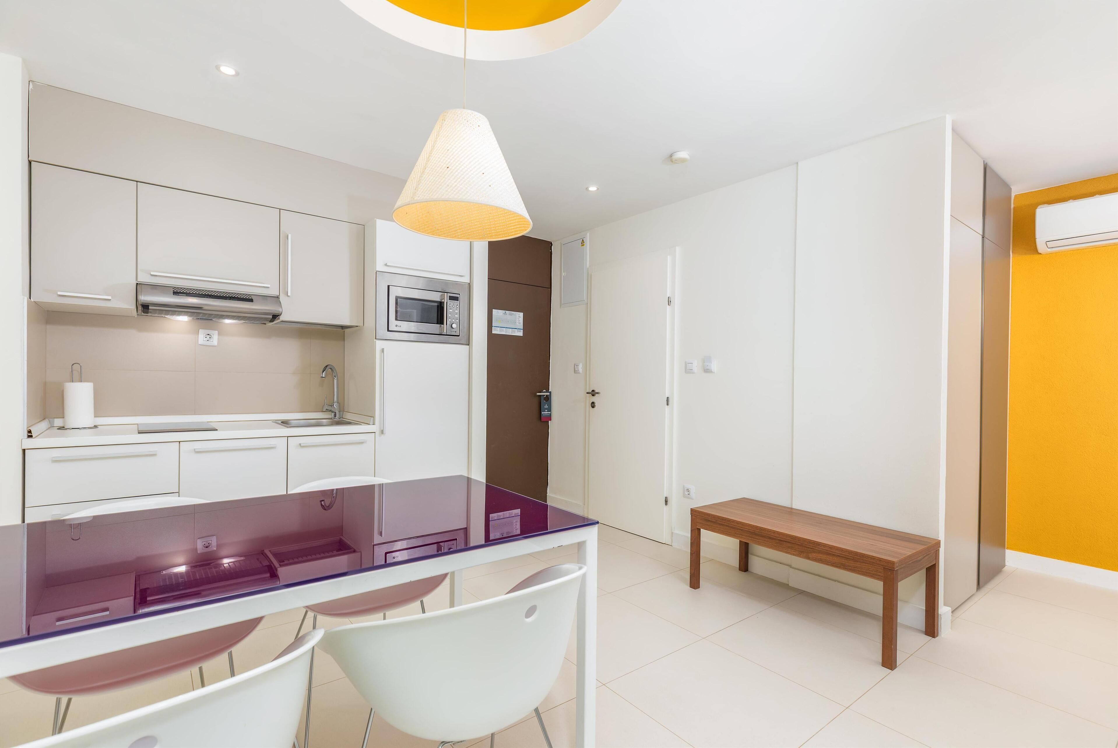 A modern kitchen with white cabinets, a microwave, and a glass-top dining table with chairs.
