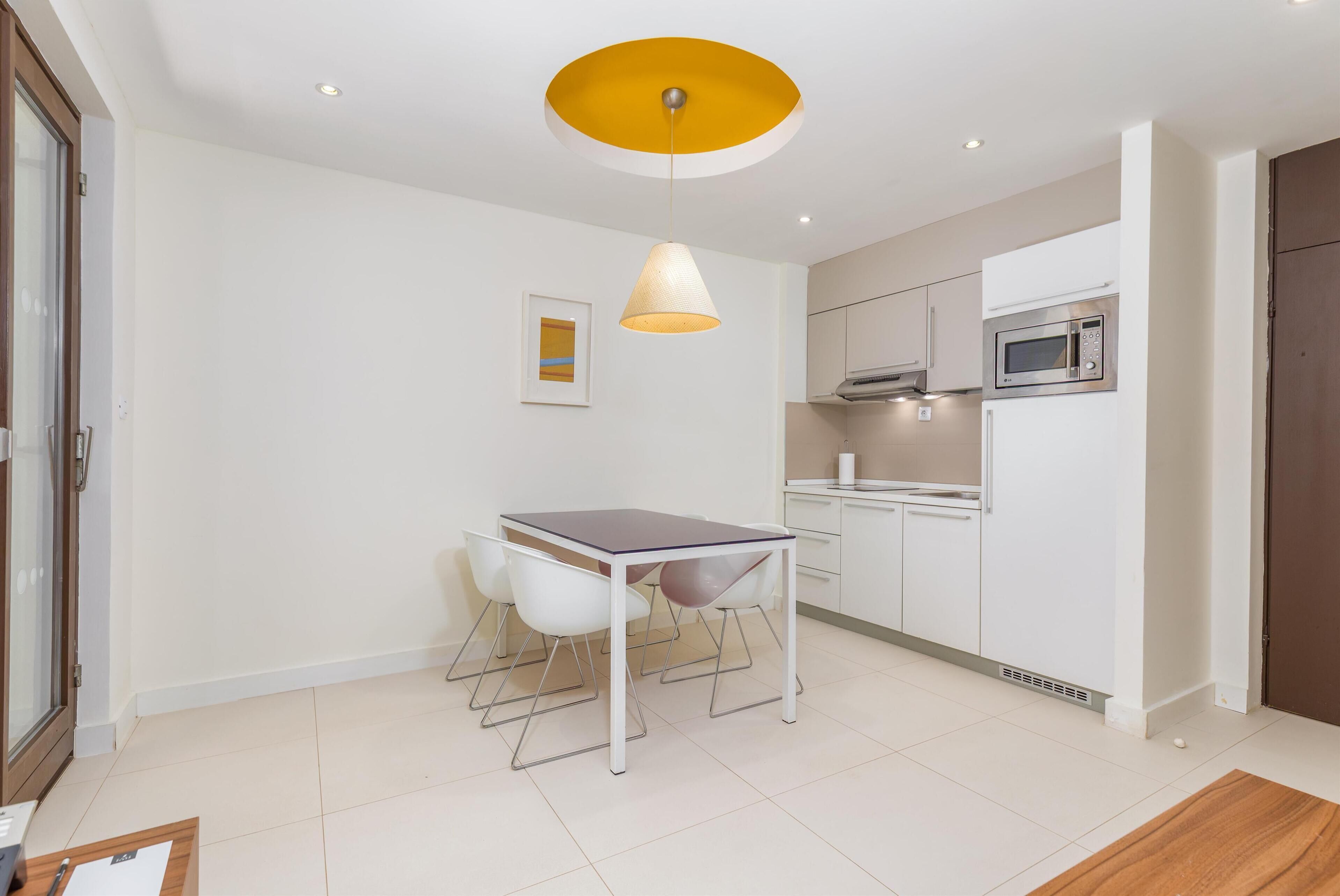 A compact kitchen with white cabinets, a microwave, and a table with chairs.