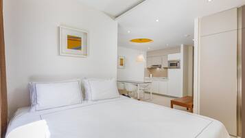 Habitación de hotel con cama, escritorio, silla, mesita pequeña, microondas y kitchenette.