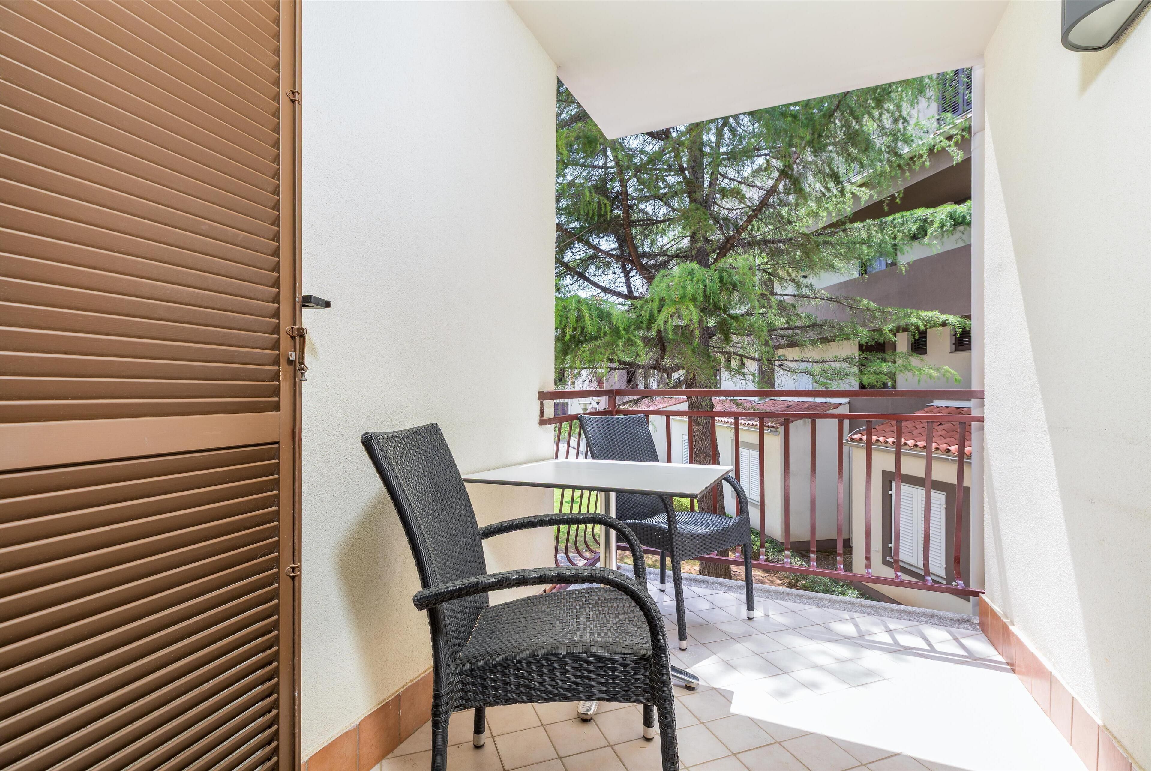 A balcony with a table and chairs, a view of trees, and a building in the background.