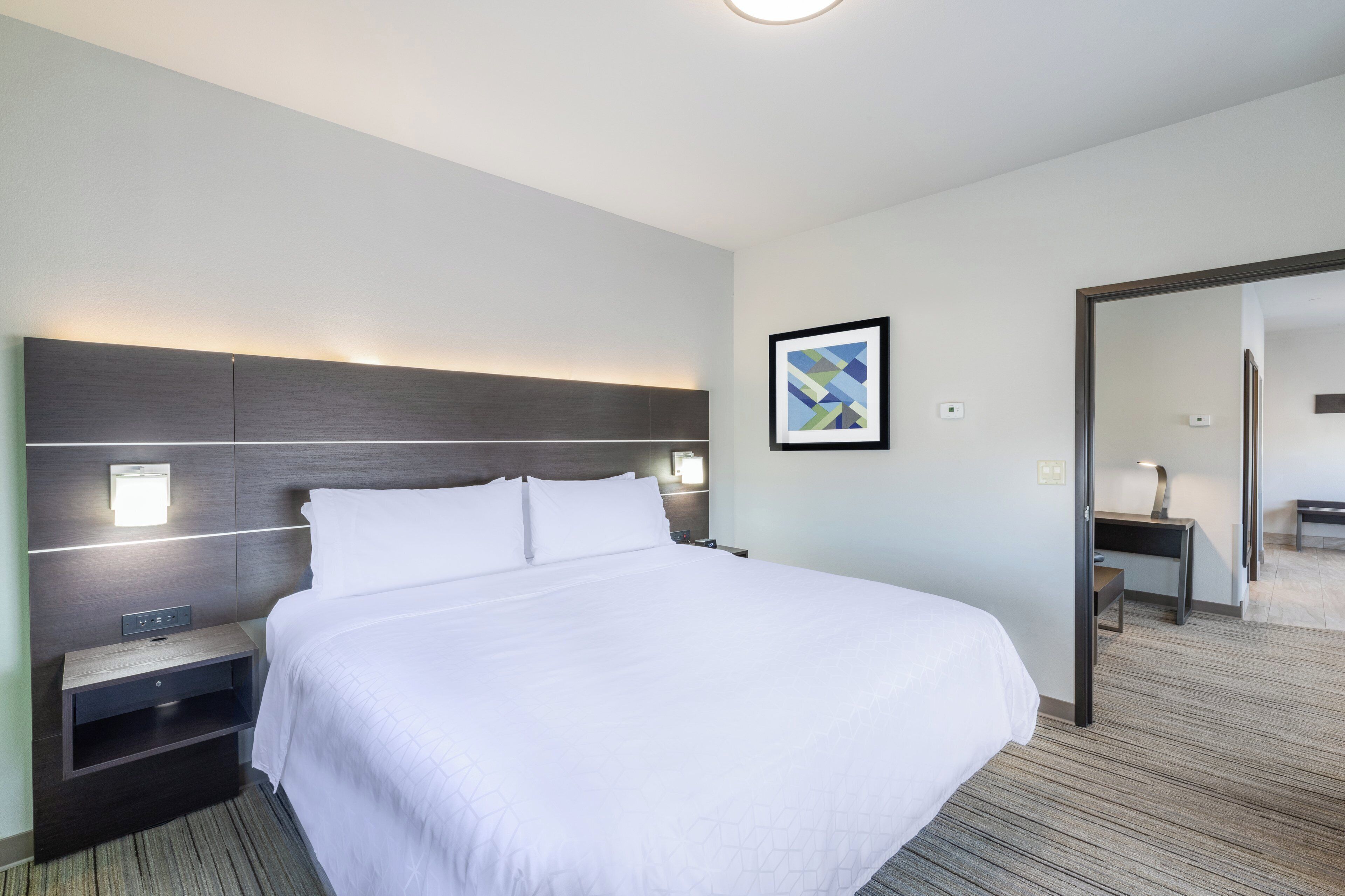 A hotel room with a large bed, bedside tables, a nightstand, a framed picture on the wall, and a mirror.