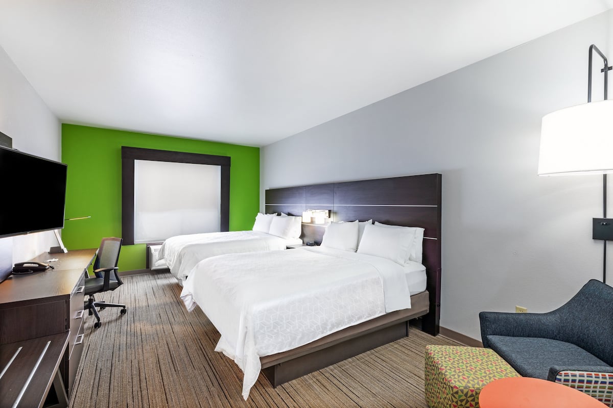A hotel room with two beds, a desk with a chair, a TV, and a sofa.