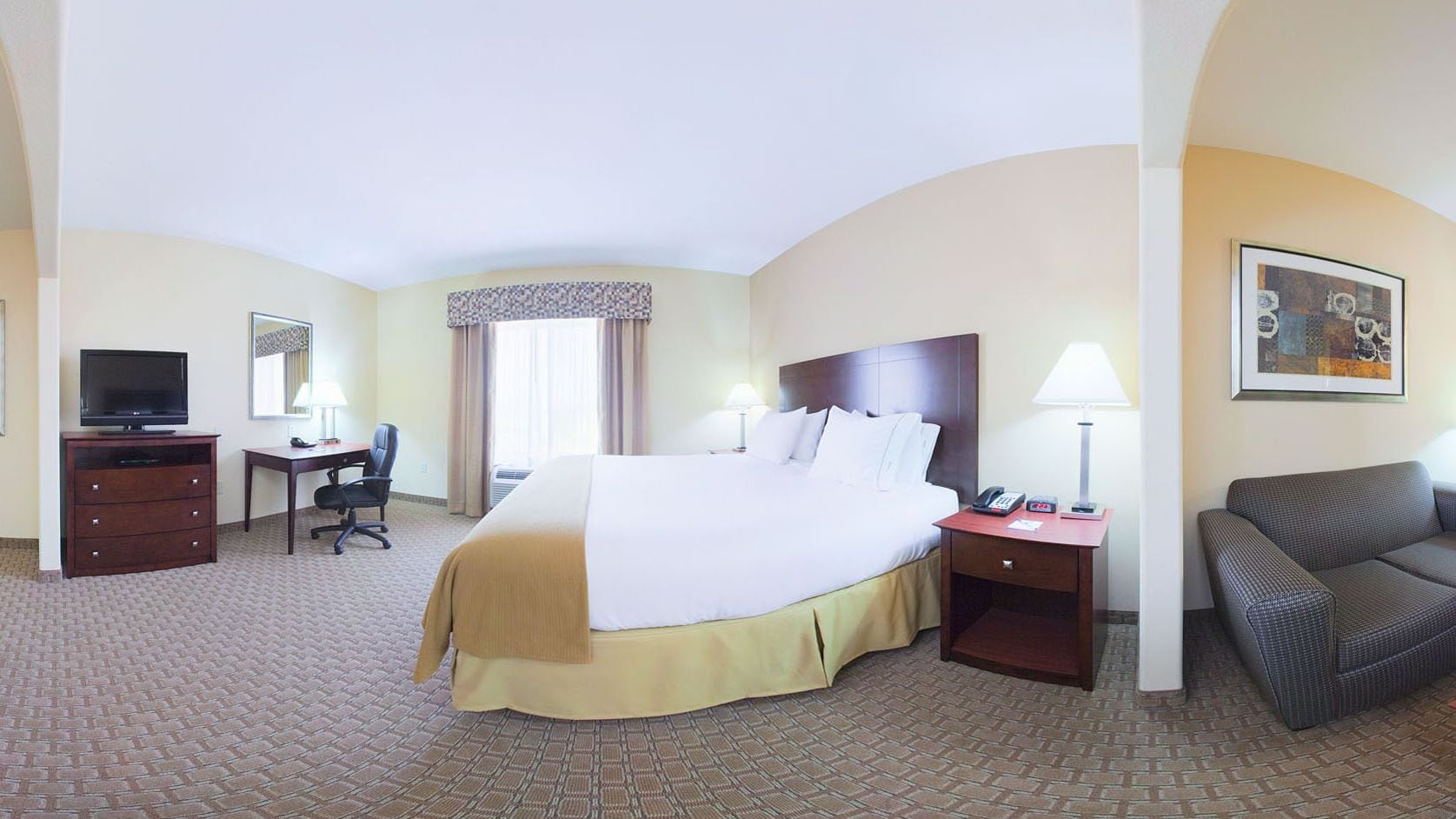 A hotel room with a large bed, a desk with a chair, a TV, a sofa, and a painting on the wall.