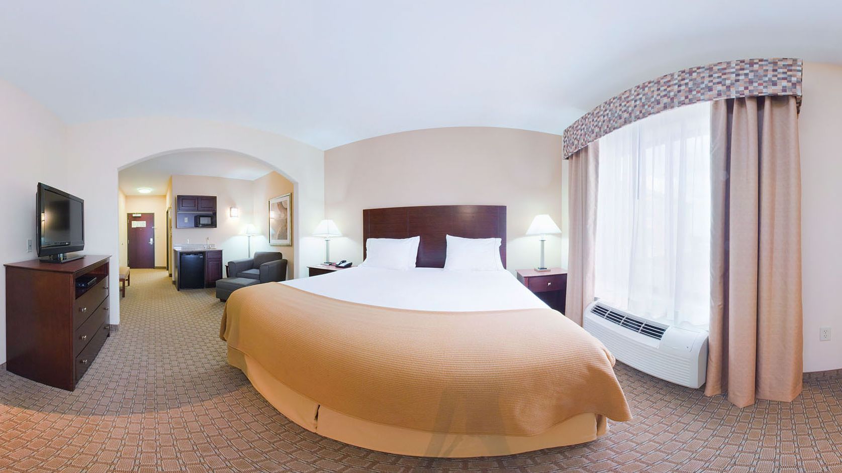 A hotel room with a large bed, a television on a dresser, a desk with a chair, and a window with curtains.