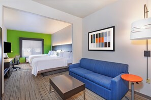 Une chambre d’hôtel avec un lit, un canapé bleu, un bureau avec une chaise, un téléviseur à écran plat et un tableau représentant une palette de couleurs accroché au mur.