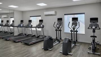 Un gimnasio con cintas de correr, máquinas elípticas y bicicletas estáticas dispuestas en filas.