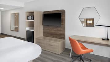 Una habitación de hotel moderna con una cama, un aparador de madera, un escritorio con una silla, un televisor de pantalla plana, un espejo y un microondas.