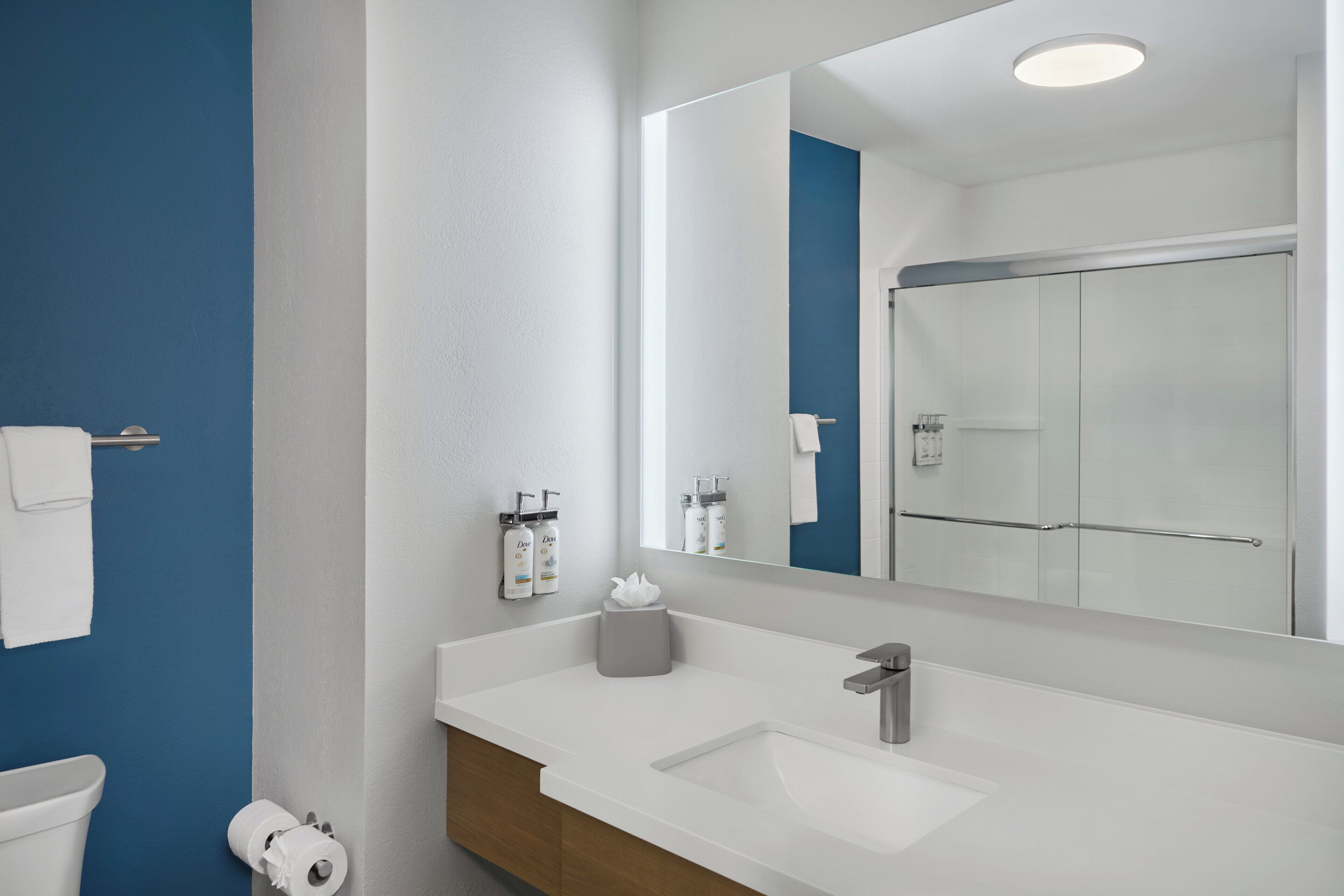 A modern bathroom with a white sink, a large mirror, and a blue accent wall.