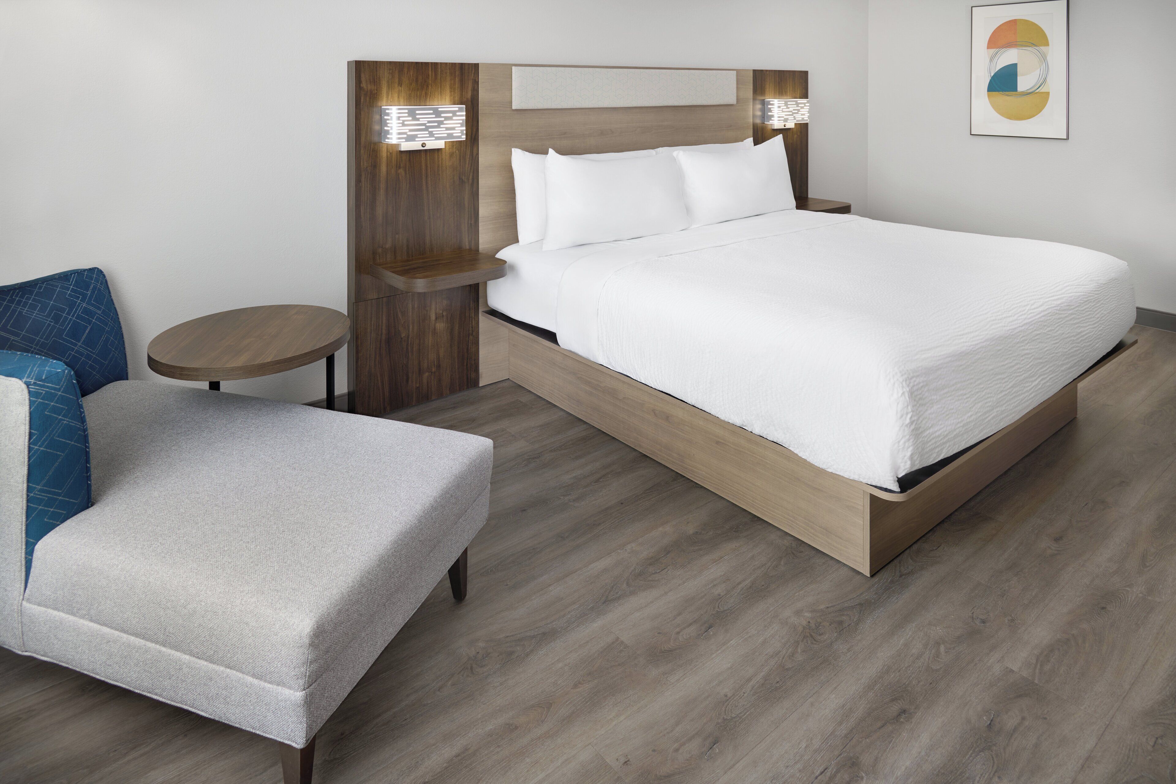 A modern hotel room with a large bed, a small round table, and a seating area with a chair.