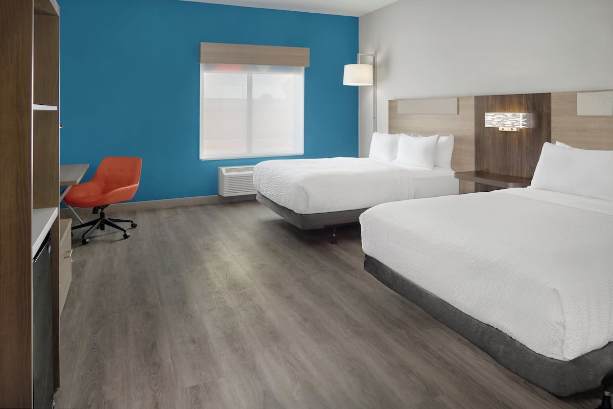 A hotel room with two beds, a desk, a chair, and a window with blinds.