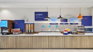 A modern breakfast bar with a blue sign reading "EXPRESS START BREAKFAST," a coffee machine, a fruit display, and a bread display. - Holiday Inn Express Hotel & Suites Odessa by IHG (Odessa)