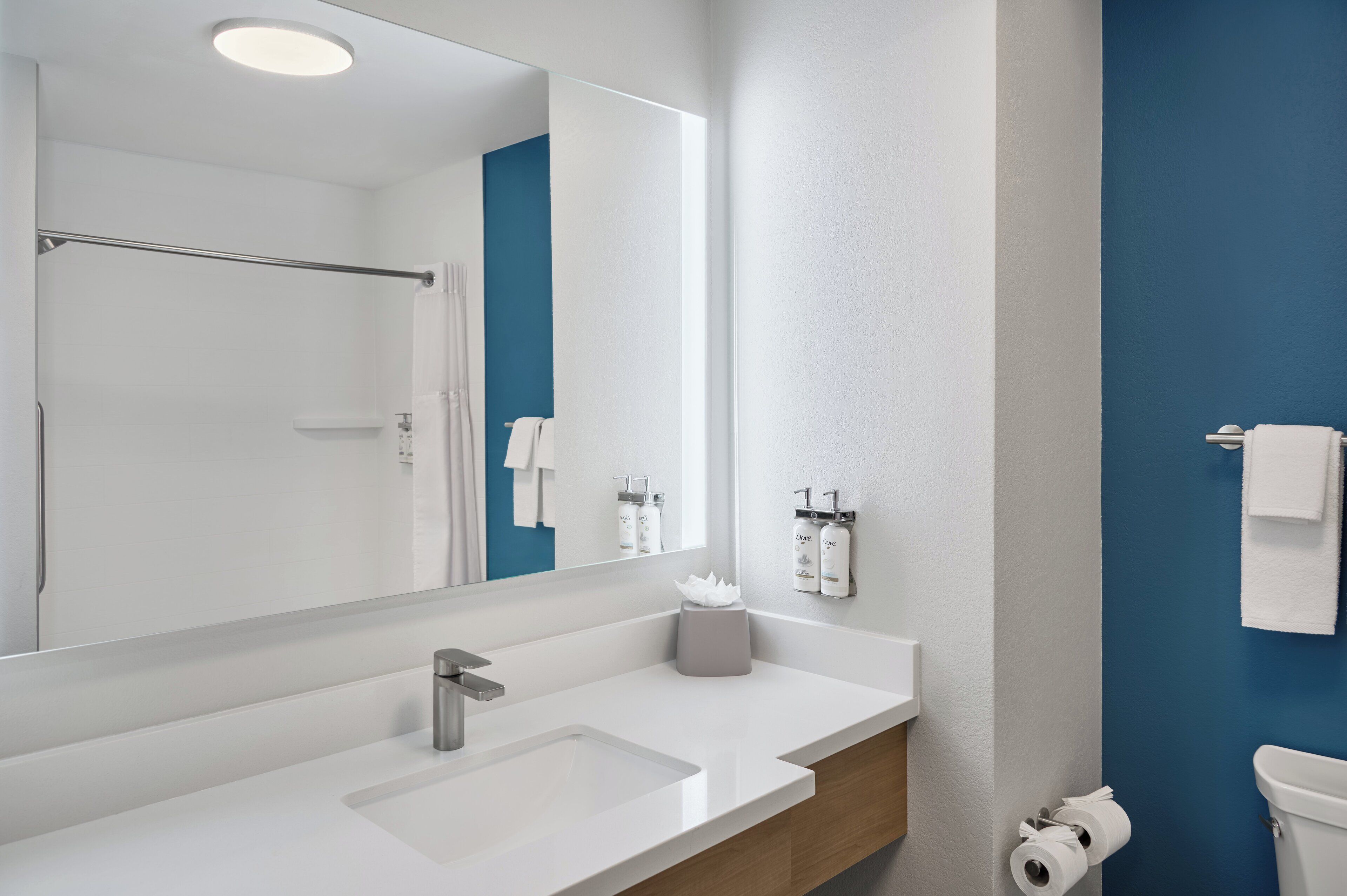Une salle de bain moderne avec un grand miroir, un lavabo blanc et un mur d’accent bleu.