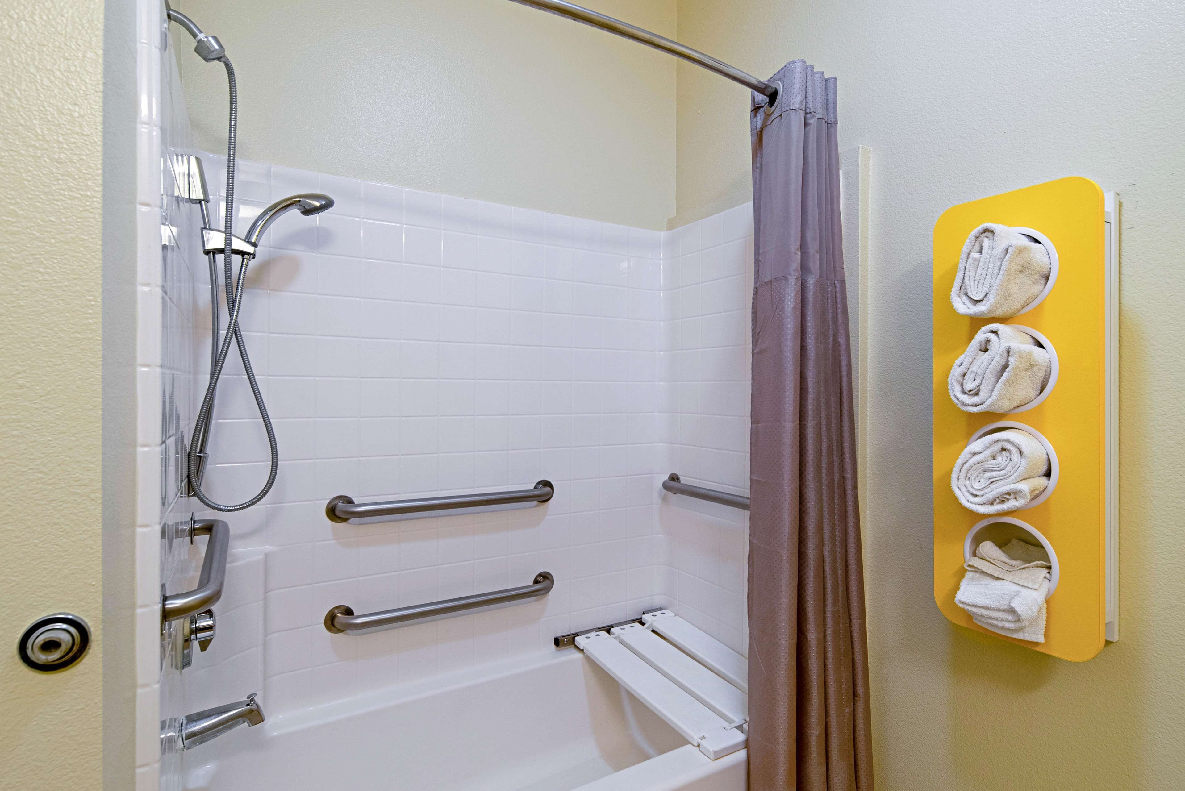 A bathroom with a white bathtub, grab bars, a showerhead, and a towel rack with towels.