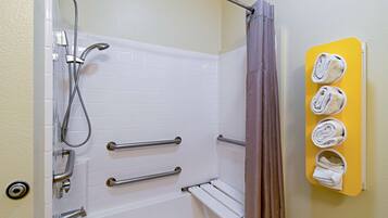 A bathroom with a white bathtub, grab bars, a showerhead, and a towel rack with towels.