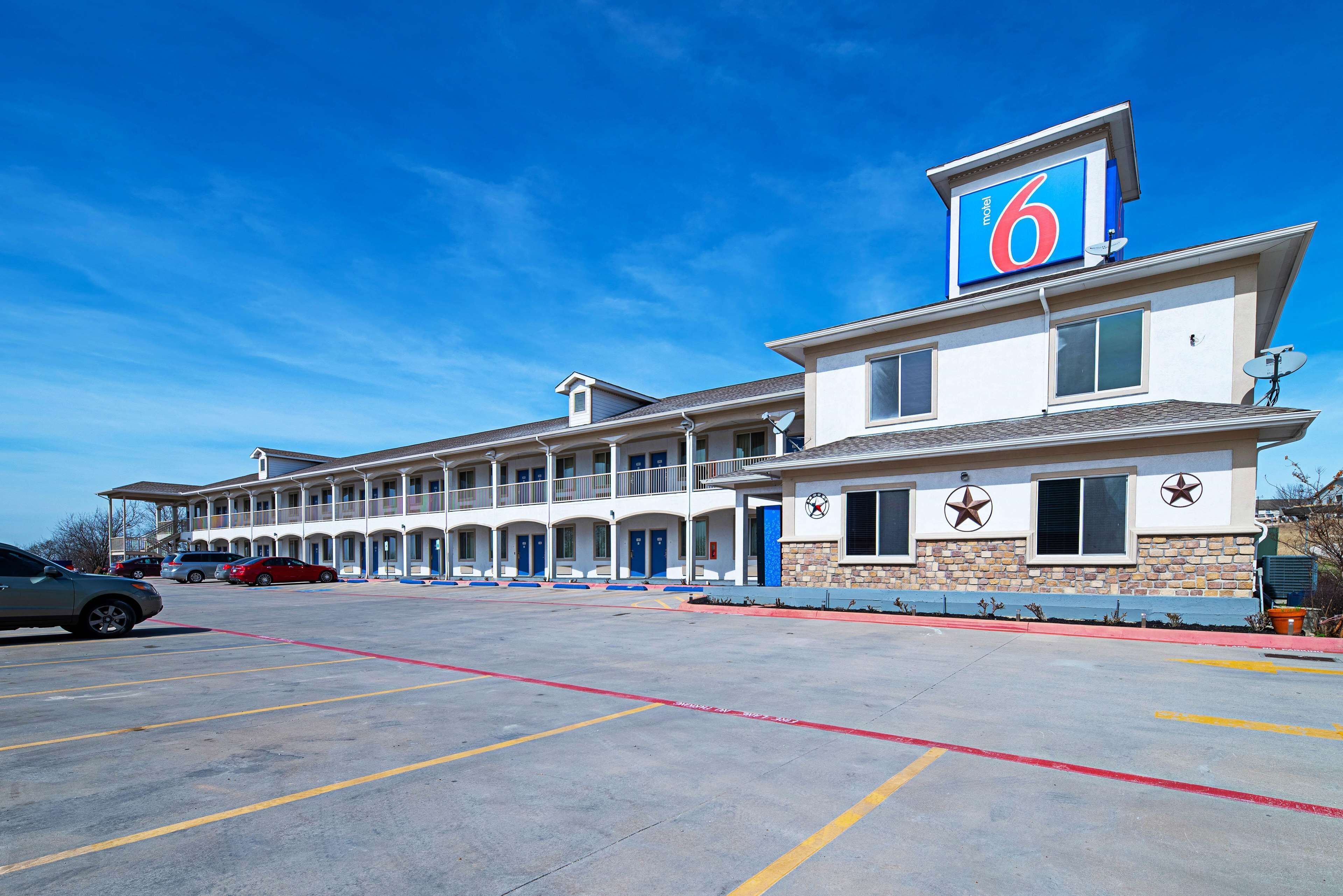 A motel with a row of rooms, a parking lot, and a clear blue sky.