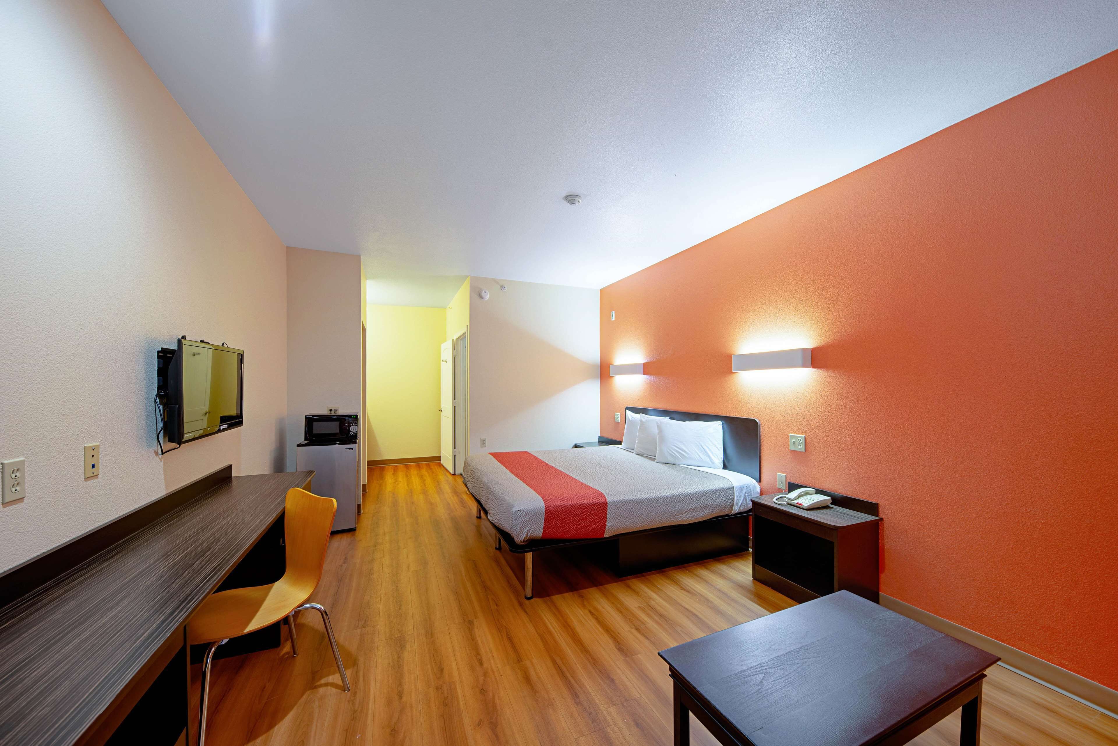 Ein Hotelzimmer mit Bett, Schreibtisch, Stuhl, einer kleinen Küchenzeile und einem an der Wand montierten Fernseher.