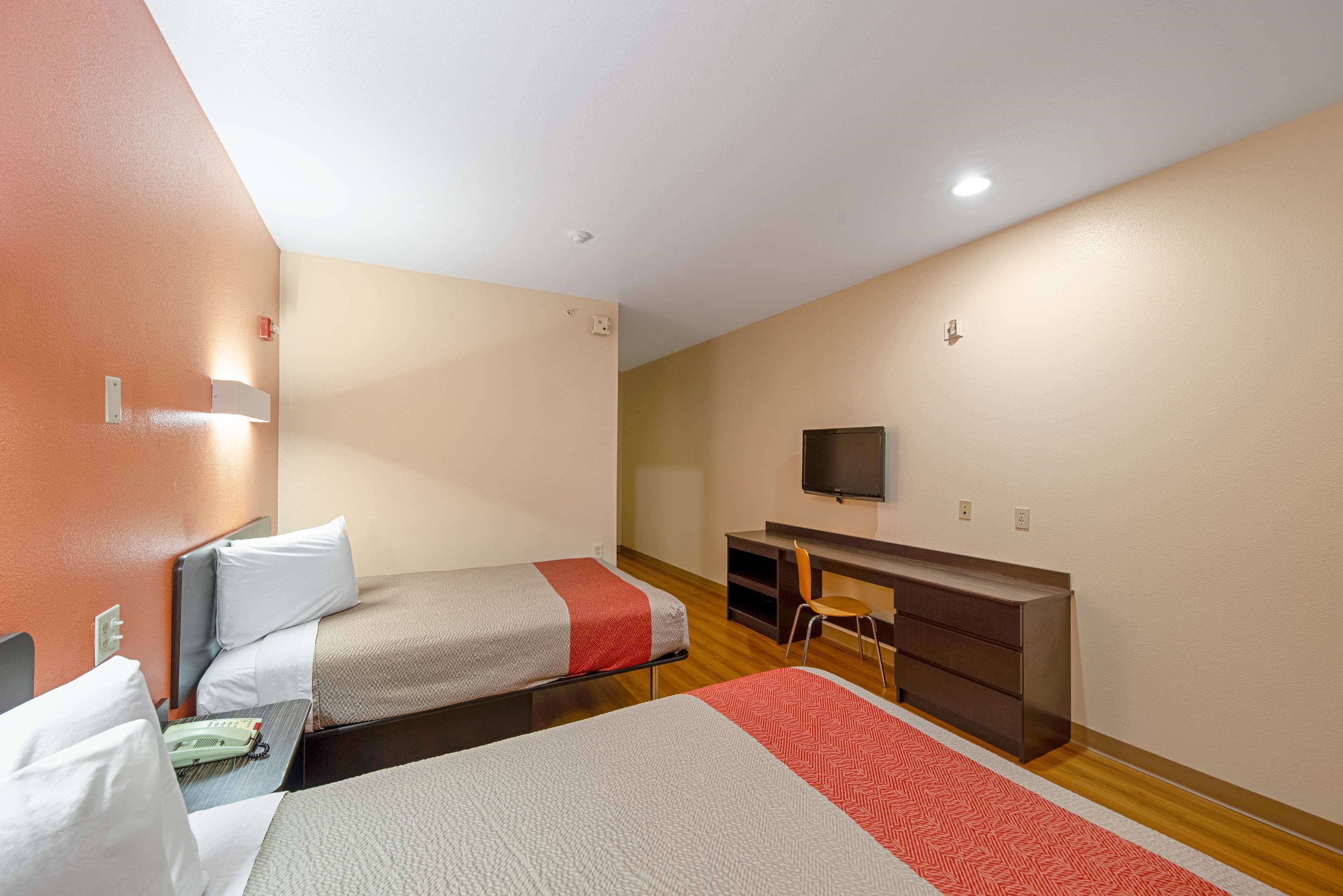 A hotel room with two beds, a desk, a chair, and a television on the wall.
