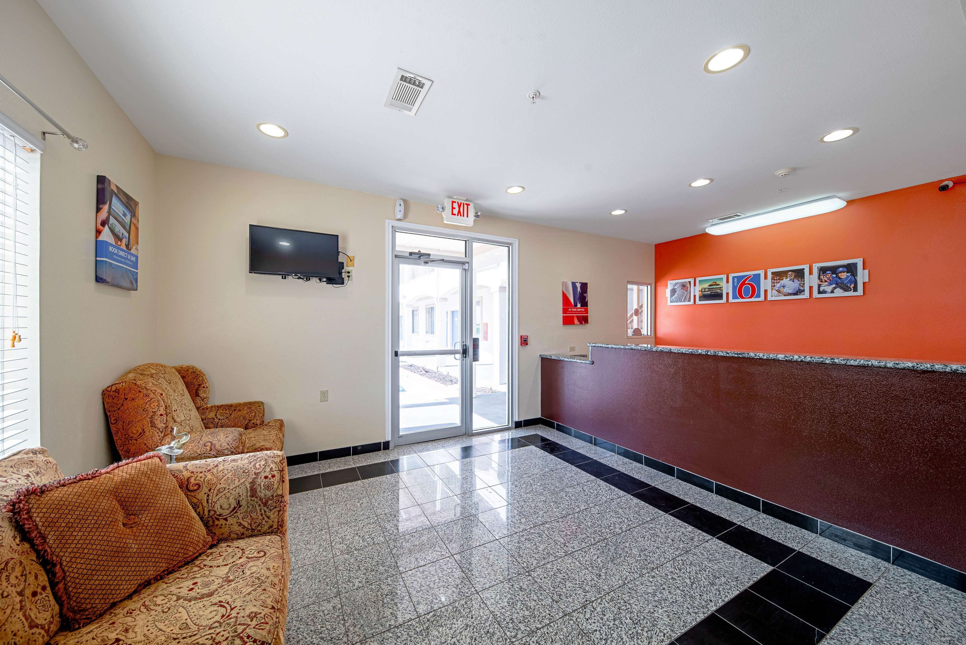 A hotel lobby with a reception desk, a television mounted on the wall, and a set of patterned sofas.