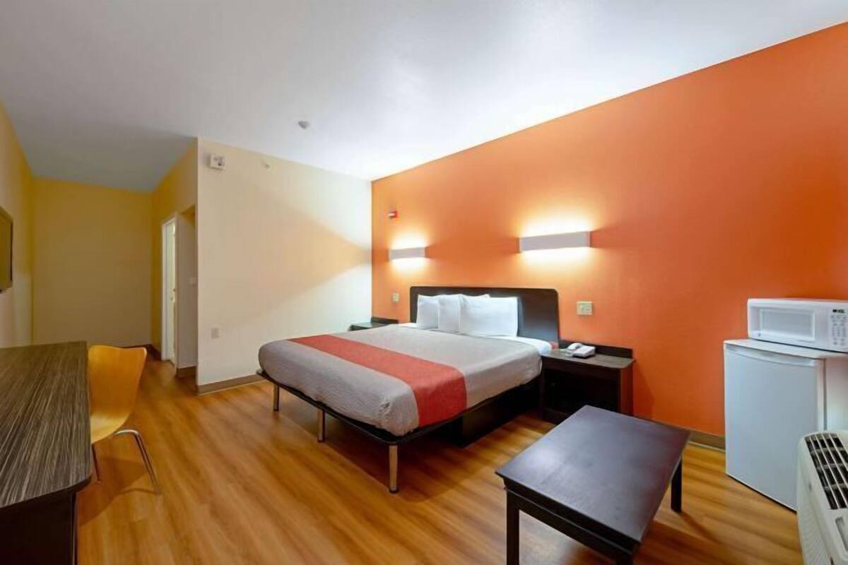 A hotel room with a bed, a desk, a chair, a microwave, and a small refrigerator.