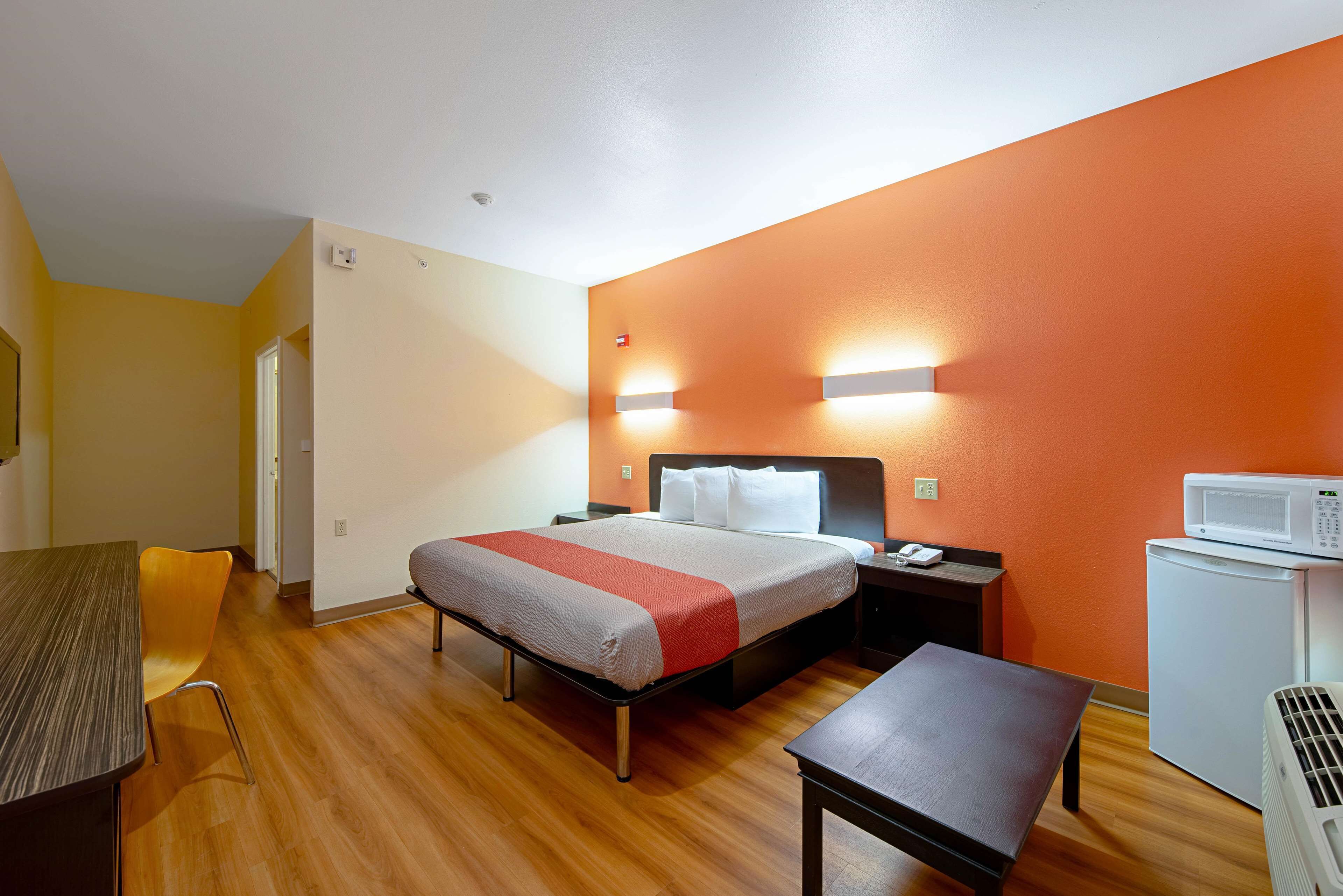 Habitació d'hotel amb llit, taula de nit, cadira, escriptori i microones.