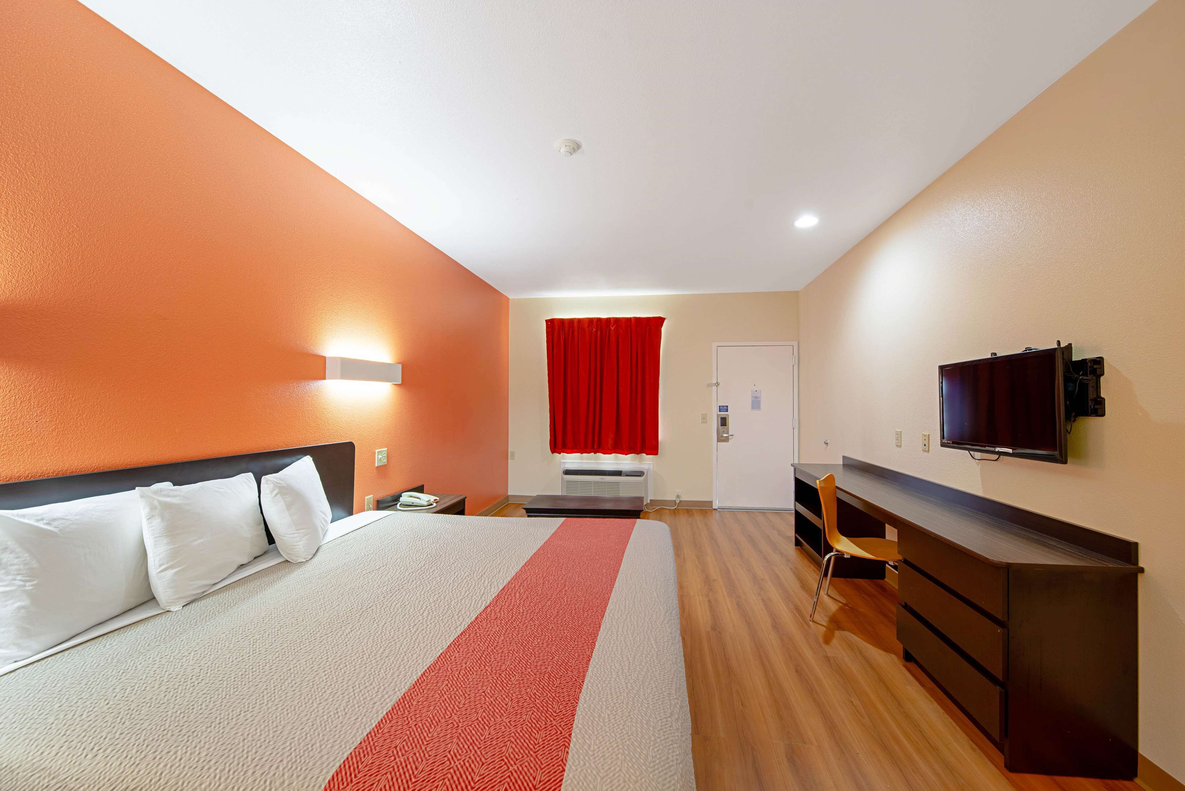 A hotel room with a bed, a desk, a chair, a TV, and a red curtain.