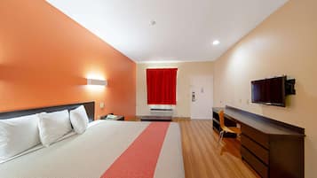 A hotel room with a bed, a desk, a chair, a TV, and a red curtain.