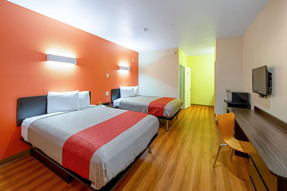 A hotel room with two beds, a desk, and a TV.