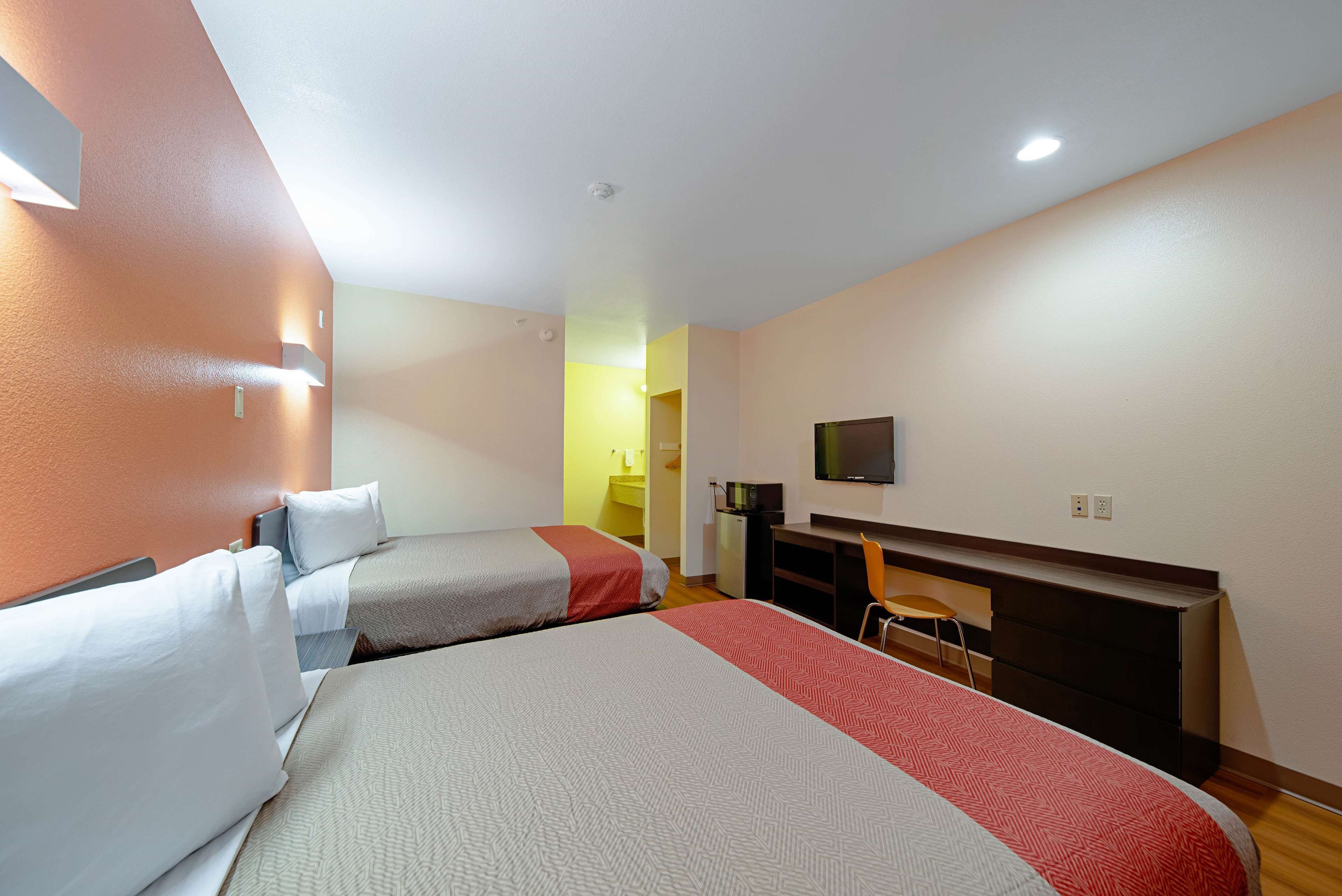 Une chambre d’hôtel avec deux lits, un bureau, une chaise, une télévision et une salle de bain visible à travers une porte ouverte.