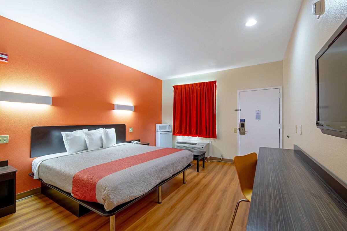 A hotel room with a bed, desk, chair, and a TV.
