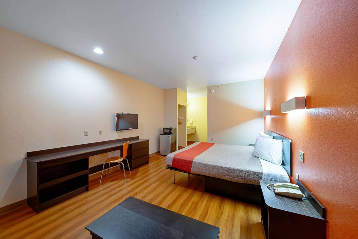 A compact hotel room with a bed, a desk, a chair, a TV, and a phone on the bedside table.