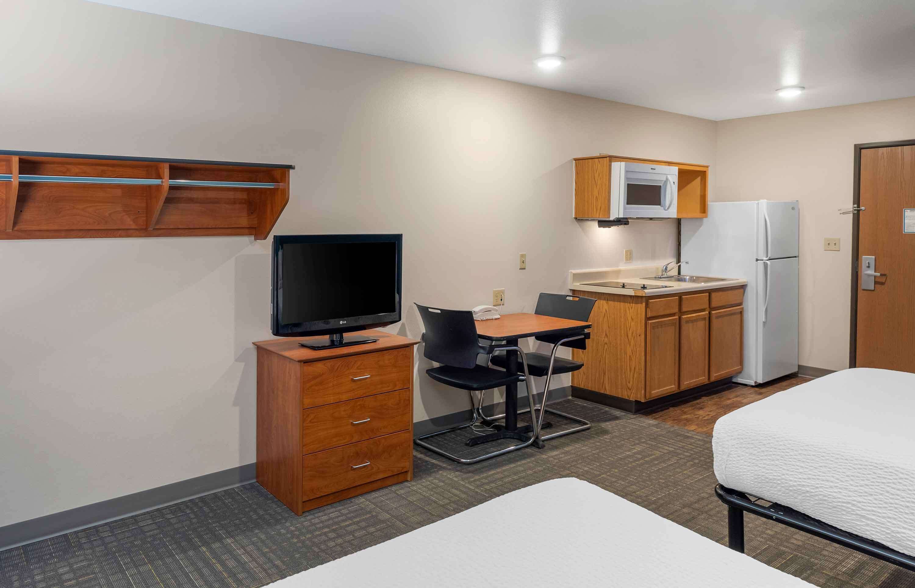 Een compacte hotelkamer met een kitchenette, een enkel bed, een bureau met stoel, een televisie en een magnetron.