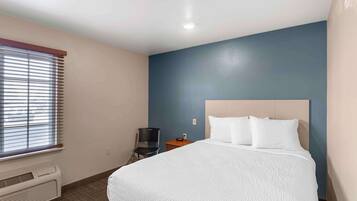 Una habitación de hotel con cama, una silla, una mesita y una ventana con persianas.