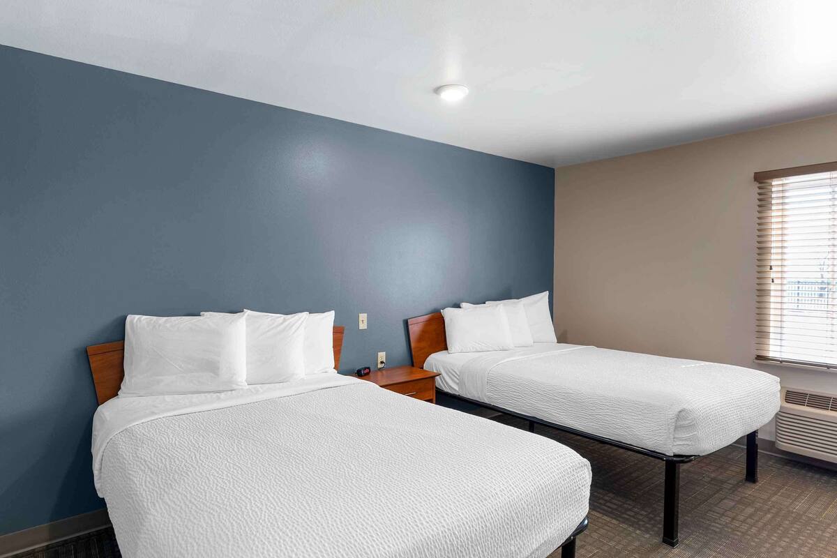 Habitación de hotel con dos camas, cabecero de madera, mesita de noche y ventana con persianas.