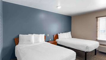 A hotel room with two beds, a wooden headboard, a nightstand, and a window with blinds.