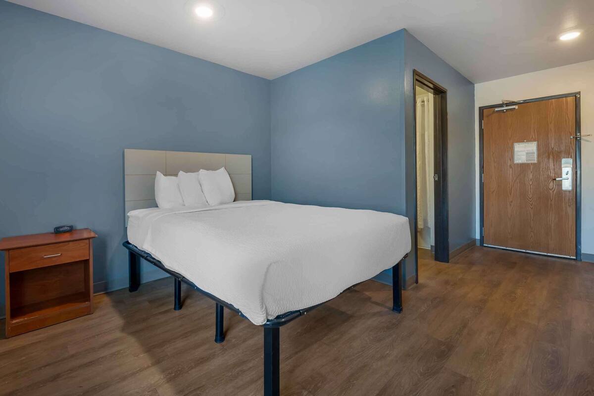 Un dormitorio con cama, mesita de noche, puerta de madera y pared azul.