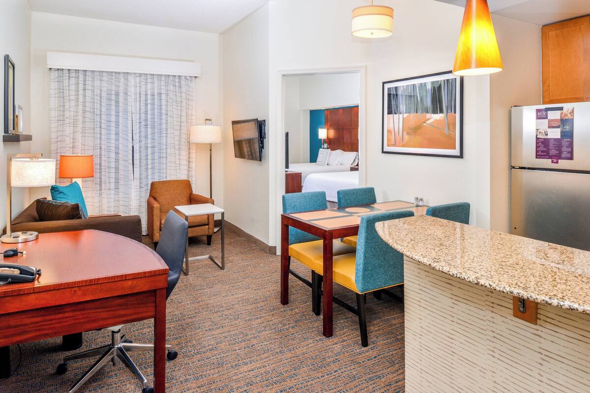 A hotel room with a dining area, a kitchen, and a bed.