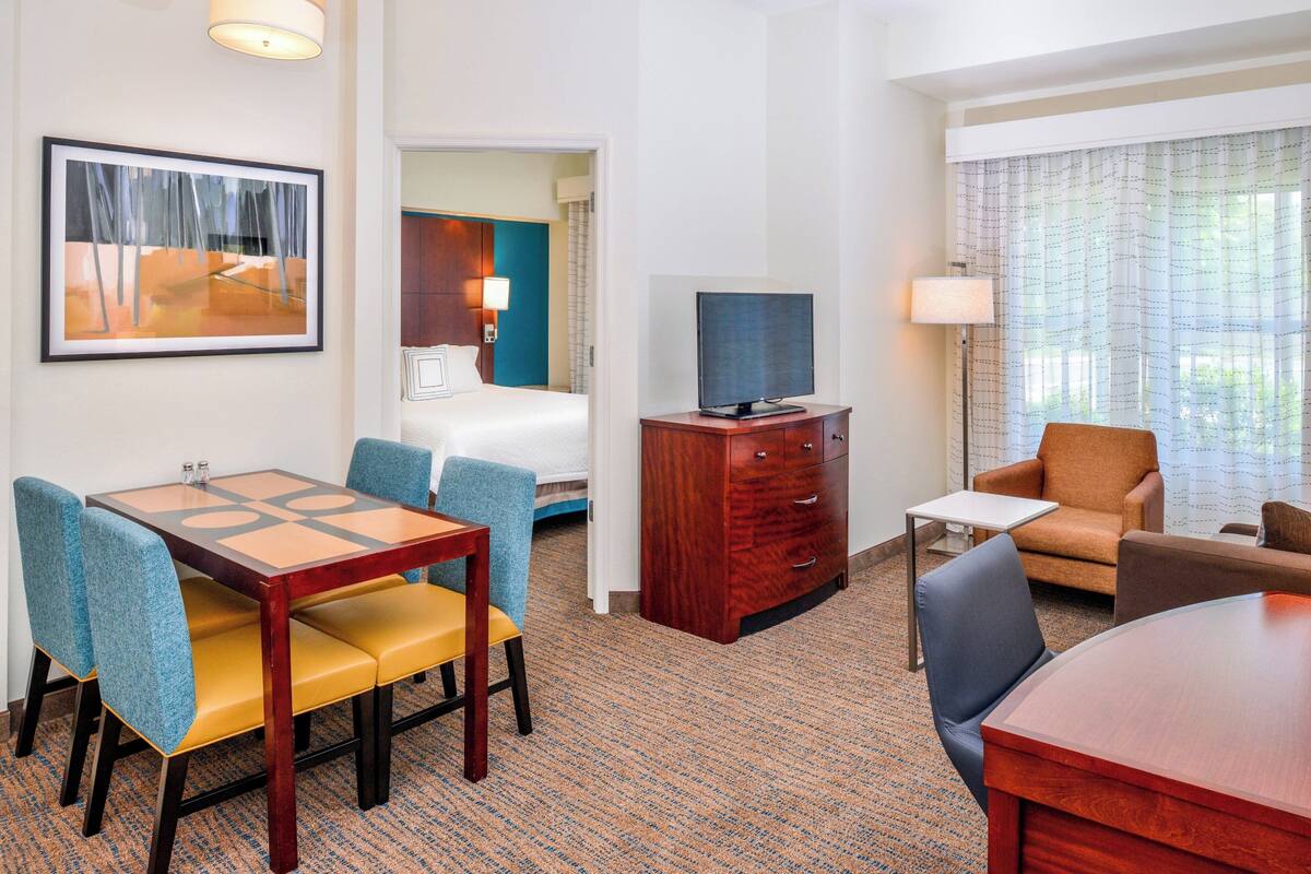 A hotel room with a dining table, chairs, a television, a desk, and a sofa.