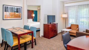 A hotel room with a dining table, chairs, a television, a desk, and a sofa.