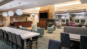 A spacious hotel lobby with a long dining table, comfortable seating, a stone fireplace, and a television mounted on the wall. - Residence Inn Marriott Waynesboro (Waynesboro)