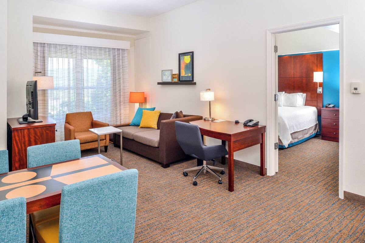 A hotel room with a sofa, a desk, a TV, and a bed.