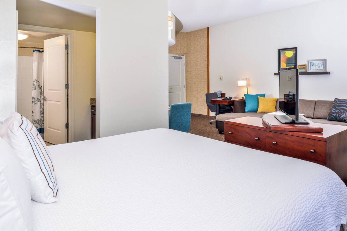 A hotel room with a large bed, a desk with a chair, a sofa, a mirror, and a lamp.