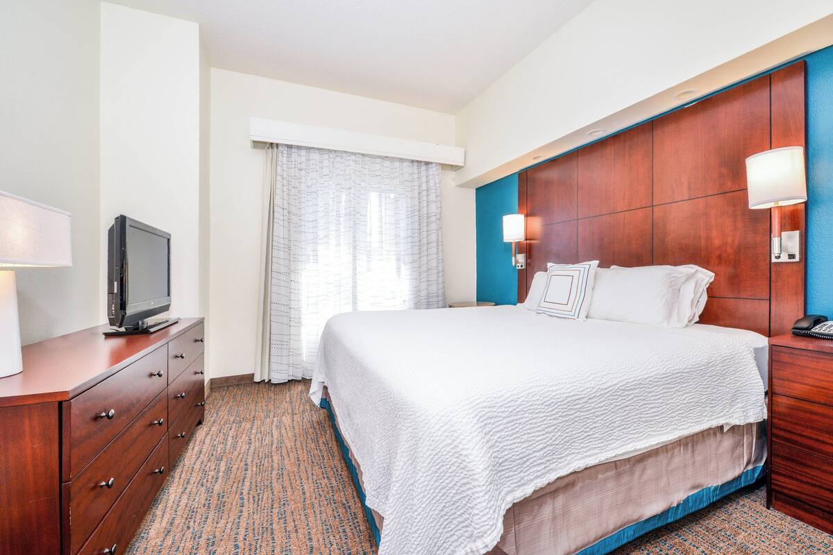 A hotel room with a large bed, a TV on a wooden dresser, and a window with curtains.