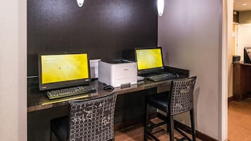Un espacio de trabajo con dos computadoras de escritorio, una impresora y dos sillas estampadas.