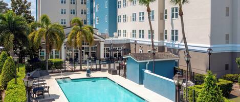 A hotel with a swimming pool surrounded by palm trees and lounge chairs.