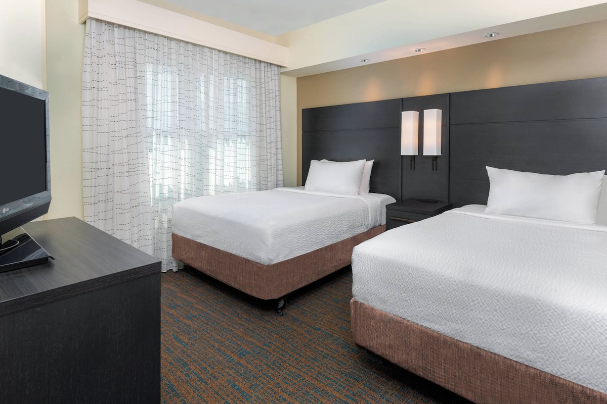 A hotel room with two beds, a desk, and a TV.